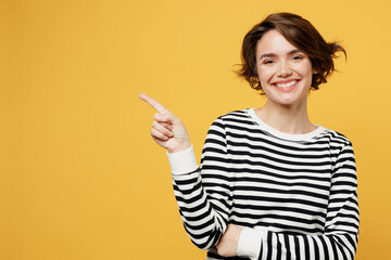 Young woman in casual striped black and white shirt point index finger aside indicate on workspace area copy space mock up isolated on plain yellow color background studio portrait Lifestyle concept - obrazy, fototapety, plakaty