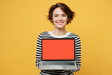 Young smiling happy fun IT woman wearing casual striped shirt hold use work on laptop pc computer...