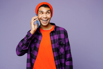 Young man of African American ethnicity wear casual shirt orange hat talk speak on mobile cell phone conducting pleasant conversation isolated on plain pastel light purple background studio portrait.