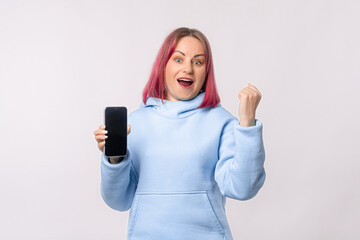 Portrait of woman with mobile phone, wins on smartphone, triumphs, winning. Winsome female model with pink hair in a blue hoodie standing over white background