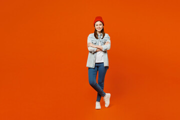 Fototapeta na wymiar Young smiling cheerful fun cool student woman wearing denim shirt white t-shirt red hat looking camera hold hands crossed folded isolated on plain orange background studio portrait. Lifestyle concept.