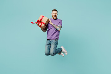 Full body excited fun young man he wears purple t-shirt jump high hold in hand present box with...