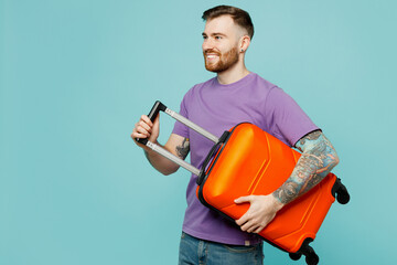 Traveler smiling man wear casual clothes hold suitcase bag isolated on plain pastel blue color background studio. Tourist travel abroad in free spare time rest getaway Air flight trip journey concept
