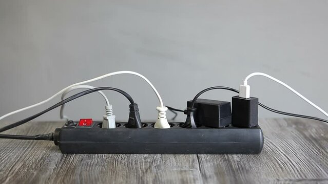A man cuts an electric wire coming from an electric extension cord with scissors. The power strip is overloaded with connected appliances.