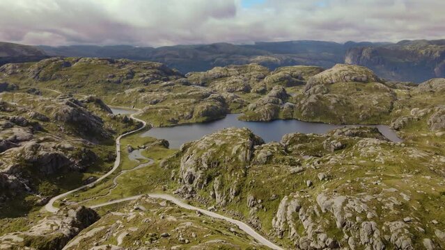Aerial view over lush, green nature and hills, towards steep mountains, landscape moving slowly while floating above glacial lakes and mountain hills. Drone shot near Lysebotn, Norway