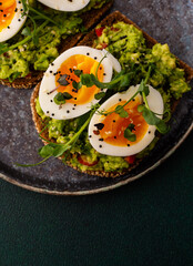 Sandwiches with rye bread and guacamole, with boiled eggs and microgreens of peas and radishes and sesame seeds, a plate with sandwiches close-up on a green background