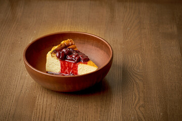 Cheesecake with cherry jam and cherries in a plate on a wooden background.
