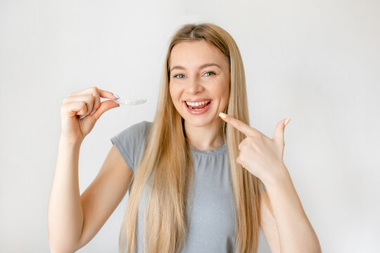 Young attractive woman holding invisible aligner orthodontic and braces pointing with hand and finger to the smile smiling happy with open mouth