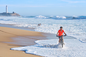 Happy senior woman cycling with her electric mountain bike at the beach of Cape Trafalgar, Costa de...