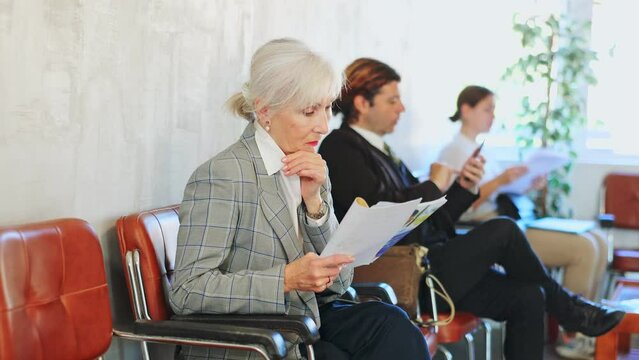 Smiling experienced female entrepreneur sitting in lobby of office with papers in hands, waiting for meeting with investors or business partner . High quality 4k footage