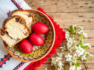 red Easter eggs next to flowering branches and plate with sweet sponge cake or cozonac on wooden...