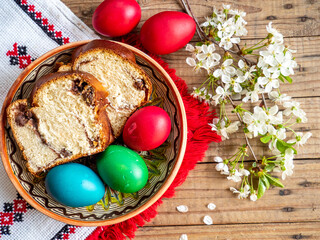 red Easter eggs next to flowering branches and plate with sweet sponge cake or cozonac on wooden table