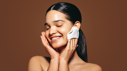 Relaxed young woman exfoliating her smooth and soft skin, she scrubs gently with a facial scrubber