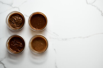 Four Different Salted Caramel sauces in glass bowls on white marble background. Butter, sugar with cream and salt. Top view