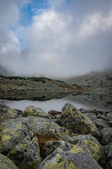 Clean, tranquil lake on top of the mountain surrounded by massive rocks and stones, vertical