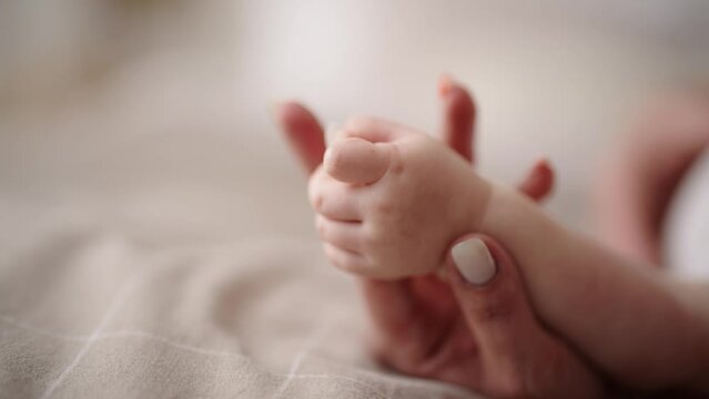 Baby touches mommy's hand grasping reflex of infants, affection formation, hands close-up view. Newborn child holding hand of mother. Childhood motherhood, babycare and kid's protection concept.