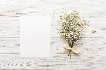 Wedding mockup with white paper list and flowers gypsophila on colored table top view flat lay....