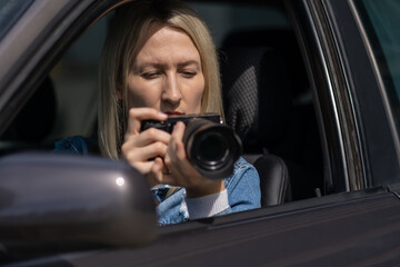 Fototapeta na wymiar Young blonde woman takes pictures sitting in a car. Concept of journalism, detective, papparation