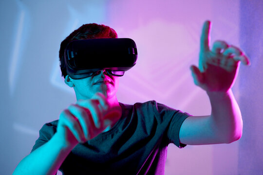 Young man wearing virtual reality simulator gesturing in front of neon wall