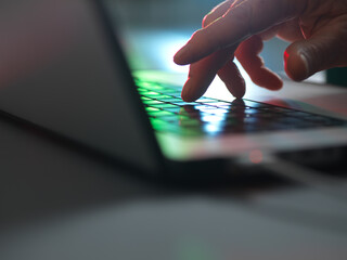Hands touching laptop keyboard in dark at home office