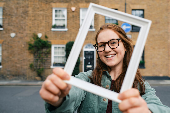 Happy young woman looking through picture frame