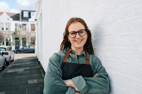 Smiling woman in apron with arms crossed leaning on wall