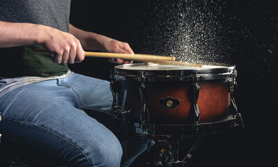 Drummer using drum sticks hitting snare drum with splashing water.