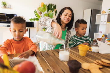 Mother pouring milk in glass by twins at dining table