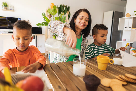 Mother pouring milk in glass by twins at dining table