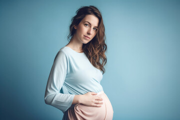 Obraz premium Expecting Joy: Pregnant Caucasian woman with hands on belly on pastel blue background with space for text. Copy space. Pregnancy and Maternity concept - AI Generative