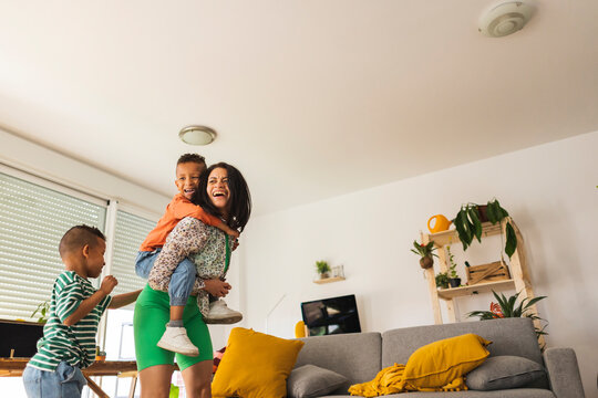 Happy mother giving piggyback ride to son at home