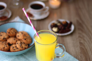 Plate of chocolate pralines, bowl of cookies, cups of tea, glasses of juice and lit candles on the table. Selective focus.