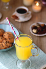Plate of chocolate pralines, bowl of cookies, cups of tea, glasses of juice and lit candles on the table. Selective focus.