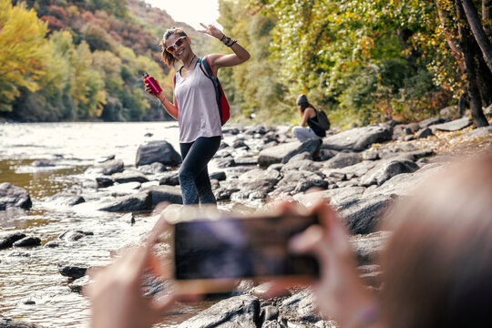 Daughter photographing mother showing peace sign standing near river