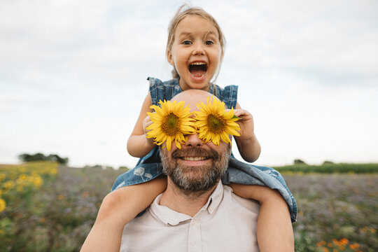 Sunflowers covering eyes of playful man with daughter in a field