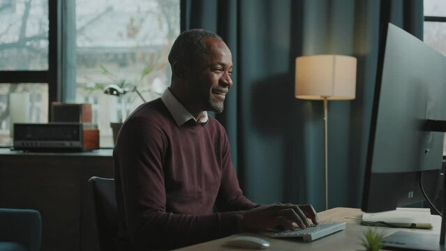 Portrait of happy emotional man sitting at computer and reading message with good news. Footage of joyful businessman working in front of monitor at home office. Indoors. Remote job