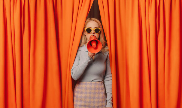 Woman talking through megaphone standing amidst orange curtains