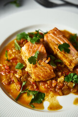Indian-style Red Salmon Curry and Fried Vegetables with a Hint of Cilantro. Asian Cuisine. Fried salmon with vegetables and green cilantro in white plate. Close up. Vertical photo 
