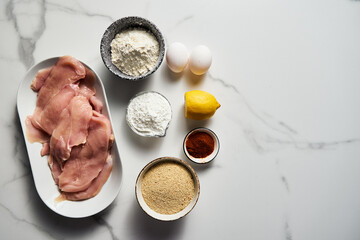 Raw Chicken fillet cut into schnitzel on an oval platter on a white marble kitchen countertop....