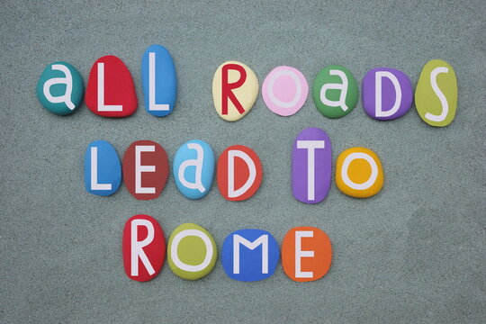 All roads lead to Rome, italian proverb composed with hand painted stone letters over green sand