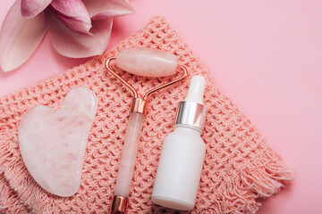 Rose quartz crystal facial roller and gua sha scraper, face serum or organic cosmetic oil on pink...