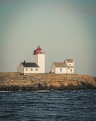 Beautiful view of a white lighthouse and houses at the seashore in a low hill