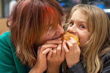 happy two girls bite off a small burger from two sides. horizontal