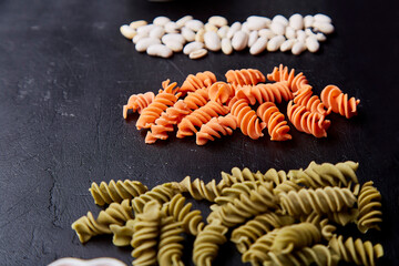 Assortment of gluten free fusilli pasta made of green pea and carrot, whole grain wheats on black...