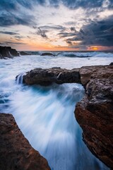 Aerial view of sea waves breaking rocky beach during sunset