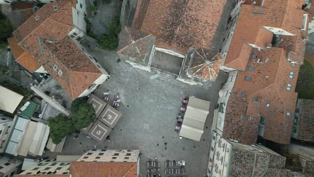 People walking over Pjaca Sv Tripuna before the St Tryphon cathedral in Kotor. Top down lifting drone shot