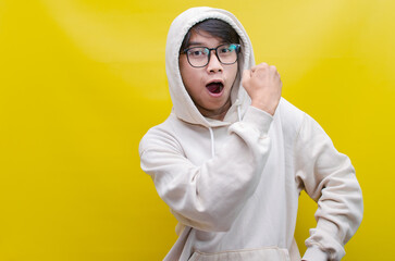 asian man in beige hoodie dancing happily and raising his fist celebrating victory