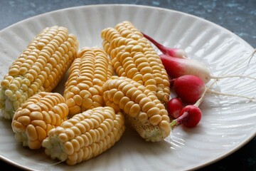 Yellow delicious boiled corn with radishes on the white plate