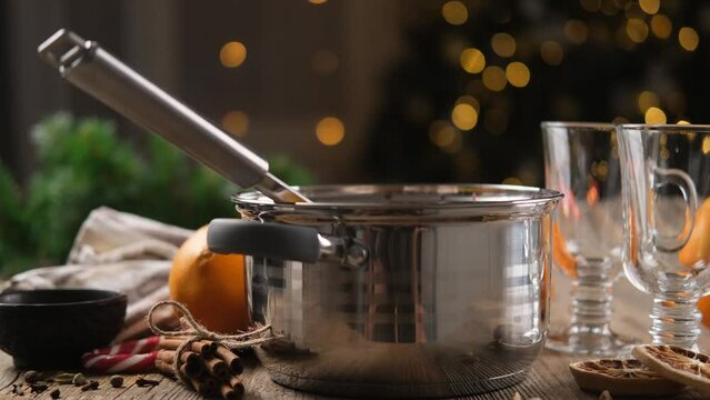 Mulled wine in pot standing on wooden table with cups and spices