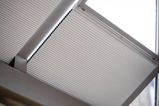 Motorized pleated blinds on the roof windows. Cellular pleated blinds for skylights, beige color. Honeycomb curtains on glass roof. Selective focus.